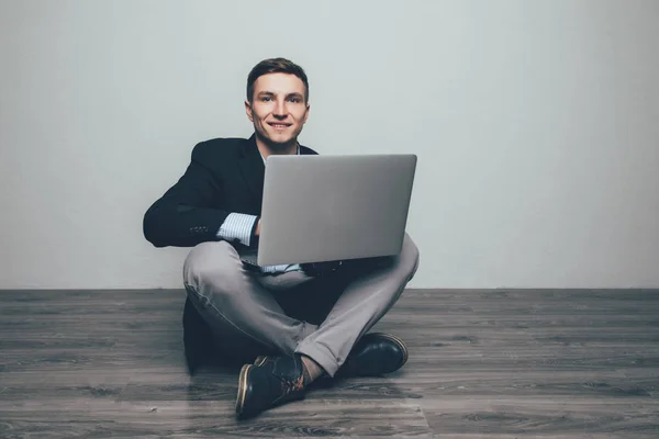 Молодий чоловік сидить на дерев'яній підлозі, використовуючи ноутбук. Концепція комунікації — стокове фото