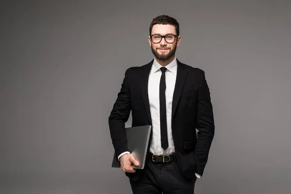 Bonito homem de negócios em óculos e terno segurando laptop em mãos vista lateral isolado fundo cinza — Fotografia de Stock