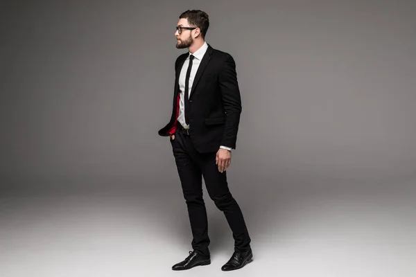 グレー上に分離されて立っているサングラスに自信を持って若いビジネスマンの完全な長さ — ストック写真