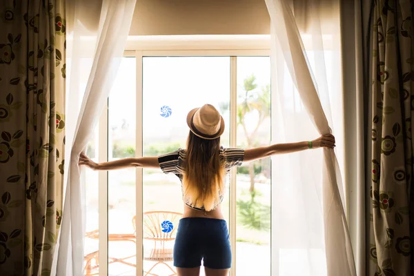 girl in hat opens the curtains, Summer morning in hotel room