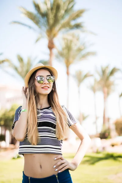 Sorrindo muito jovem mulher de chapéu e óculos de sol de pé e relaxante no resort de verão — Fotografia de Stock