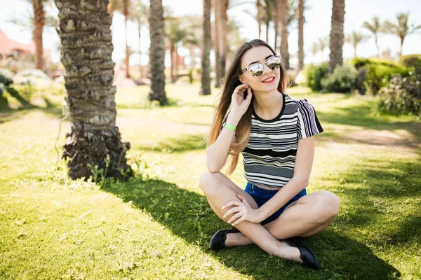 Une jeune femme assise sur l'herbe et profiter du soleil d'été sur la station. vocation estivale — Photo