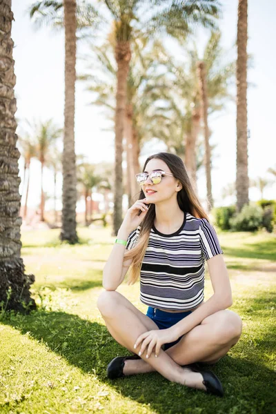 Молода жінка сидить на траві і насолоджується літнім сонцем на курорті. Літнє покликання — стокове фото
