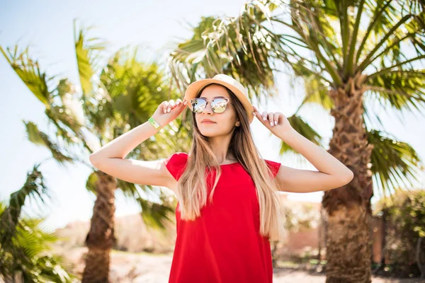 Joyeux belle jeune femme en robe rouge et chapeau marche et parler sur téléphone mobile sur la station balnéaire d'été — Photo