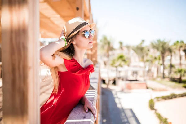 Молода біла дівчина стоїть на пірсі в червоній сонячній сукні і капелюсі . — стокове фото