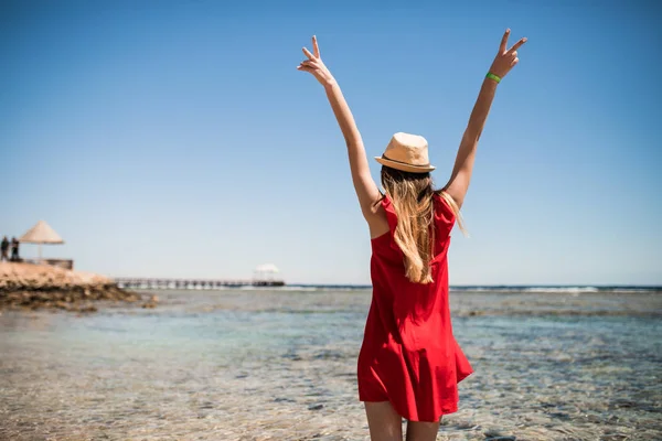 Женщина в шляпе наслаждается свободой на берегу океана с поднятыми руками на морском фоне. Летнее призвание . — стоковое фото