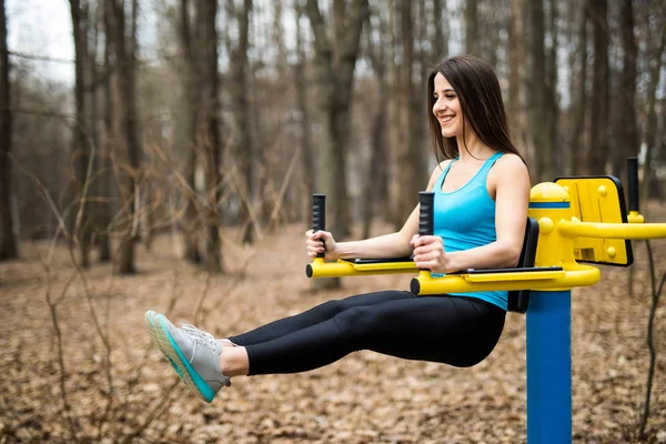 Leteszem a bordásfal vele lábak, erős fiatal nő portréja. Fitness nő végző függő láb emel a szabadtéri parkban — Stock Fotó