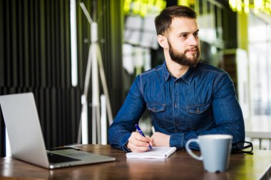 Dizüstü bilgisayarda çalışan ve kafede kahve tadını çıkarırken gülümseyen yakışıklı delikanlı