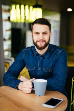 Onun yanına döşeme telefon ile masada otururken kafede zevk kahve yakışıklı genç adam