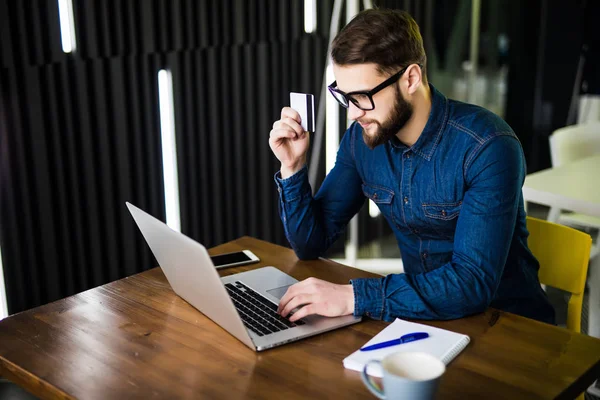 Pago en línea. Hombre sosteniendo una tarjeta de crédito y el uso de ordenador portátil en escritorio de madera para compras en línea . — Foto de Stock