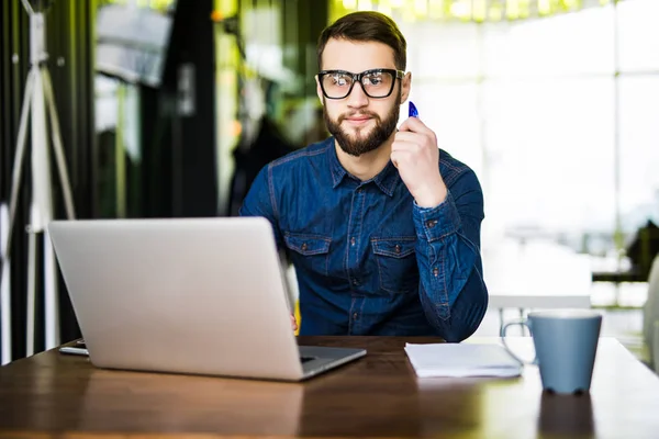 Paiement en ligne. Homme tenant une carte de crédit et utilisant un ordinateur portable sur un bureau en bois pour les achats en ligne. Regardez la caméra. — Photo