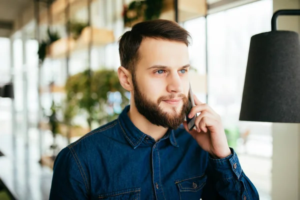 Pohledný podnikatel v běžné nošení mluví na mobilním telefonu, ukázal přitom stát v kanceláři — Stock fotografie
