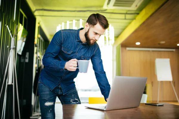 Hombre atractivo empresario de pie en su escritorio y en algo en la pantalla de su ordenador — Foto de Stock