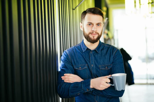 Yakışıklı adam rahat bir fincan tutarak ve uzak duran ofisinde arıyor — Stok fotoğraf