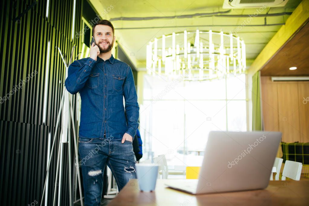 Handsome male entrepreneur standing at his desk and talking phone in office