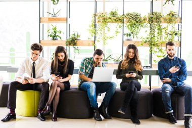 Birbirleriyle ve herkes yakınındaki sandalyelere oturan arkadaş grubu modern ofis odasında onun divices kullanın. Cihazın birlikte eğlenceli.