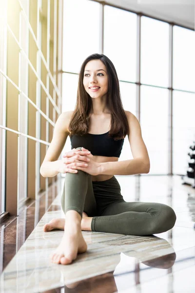 Relajante después del entrenamiento. Vista de una hermosa mujer joven mirando hacia otro lado mientras está sentada en una colchoneta de ejercicio en el gimnasio — Foto de Stock