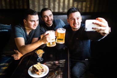 Neşeli eski arkadaşlar eğlenmeye alarak selfie ve içme taslak bira barda.