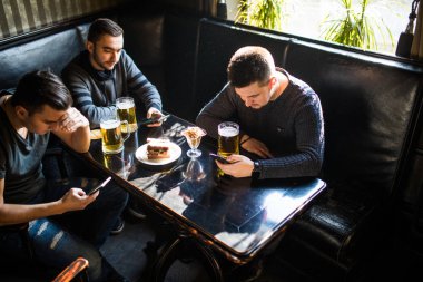 Male friends sitting in smartphones drinking beer at bar or pub. Smartphones dependence. clipart