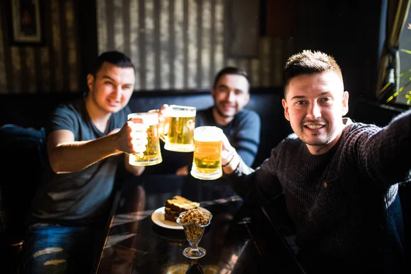 Três jovens com roupas casuais estão sorrindo, tomando selfie e bebendo cerveja enquanto estão sentados no pub. A divertir-se . — Fotografia de Stock