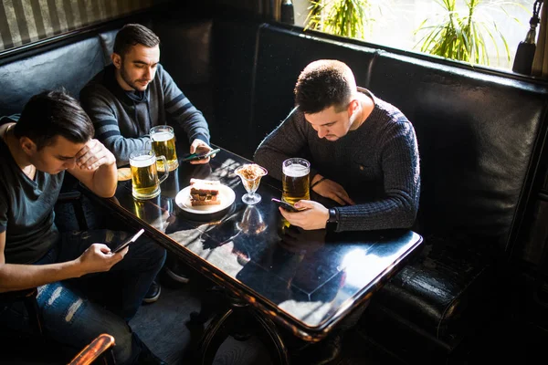 Manliga vänner sitter i smartphones som dricker öl på bar eller pub. Smartphones beroende. — Stockfoto