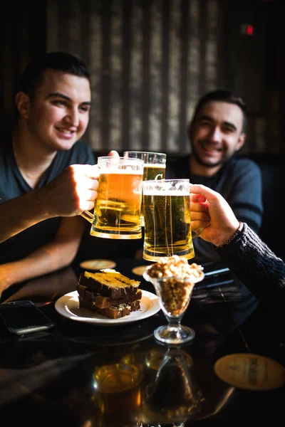 Amigos bebiendo cerveza y tintineo vasos en el bar o pub — Foto de Stock