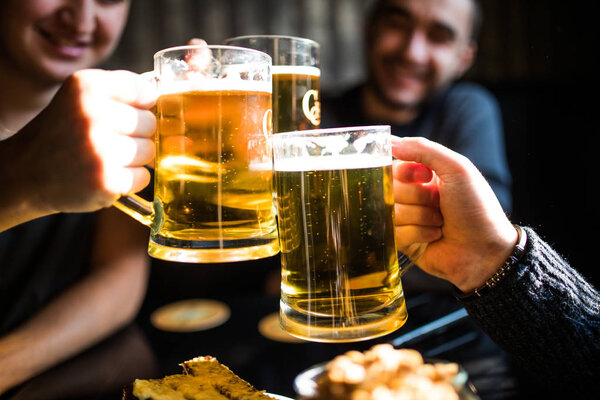 Close up of clanging glasses of beer of three friends in pub