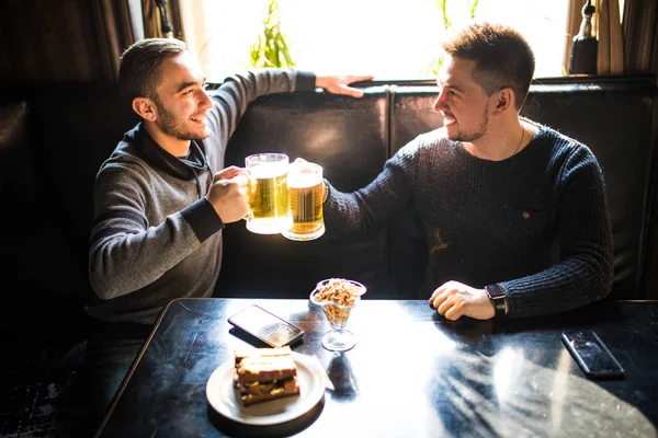 Dois jovens sentados no pub, comendo e bebendo cerveja no pub — Fotografia de Stock