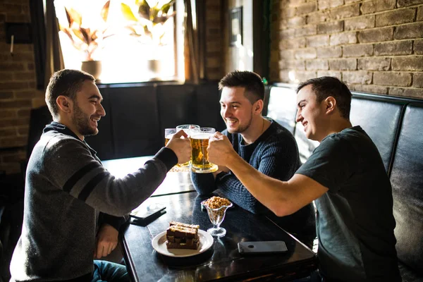 Möte med de bästa vännerna. Tre lyckliga unga män i casual wear prata och dricka öl medan du sitter i bar grupp — Stockfoto