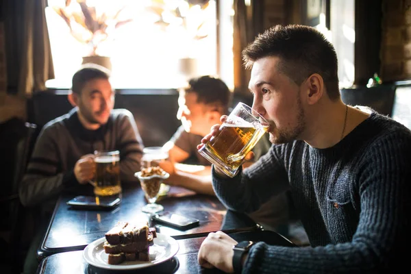 El hombre bebe cerveza frente a hablar de amigos bebiendo en el pub. Amigos en el pub . — Foto de Stock