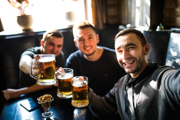 Amigos varones felices bebiendo cerveza y tomando selfie con teléfono inteligente en el bar o pub —  Fotos de Stock