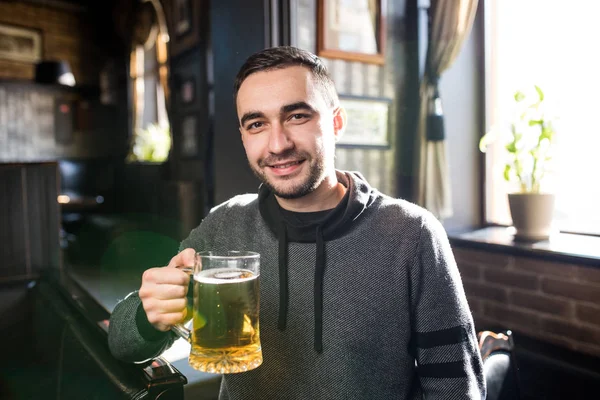 Homem bonito em um pub ou bar segurando caneca a cerveja no ar para aplausos — Fotografia de Stock