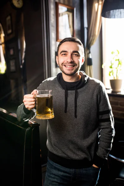 Homem bonito em um pub ou bar segurando caneca a cerveja no ar para aplausos — Fotografia de Stock