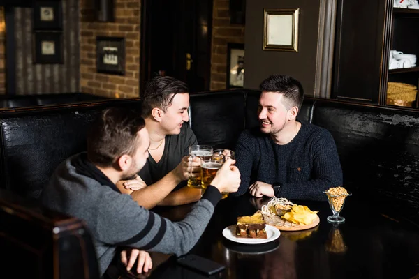 Tre killkompisar dricka öl och äta i traditionell england pub. — Stockfoto