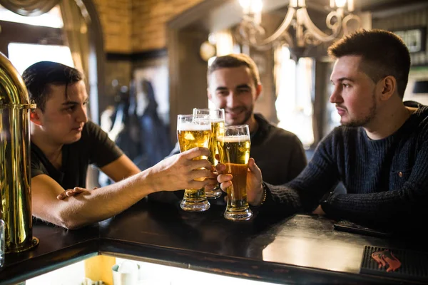 Amigos no bar. Três jovens felizes vestindo roupas casuais conversando e bebendo cerveja enquanto sentados no balcão do bar juntos — Fotografia de Stock