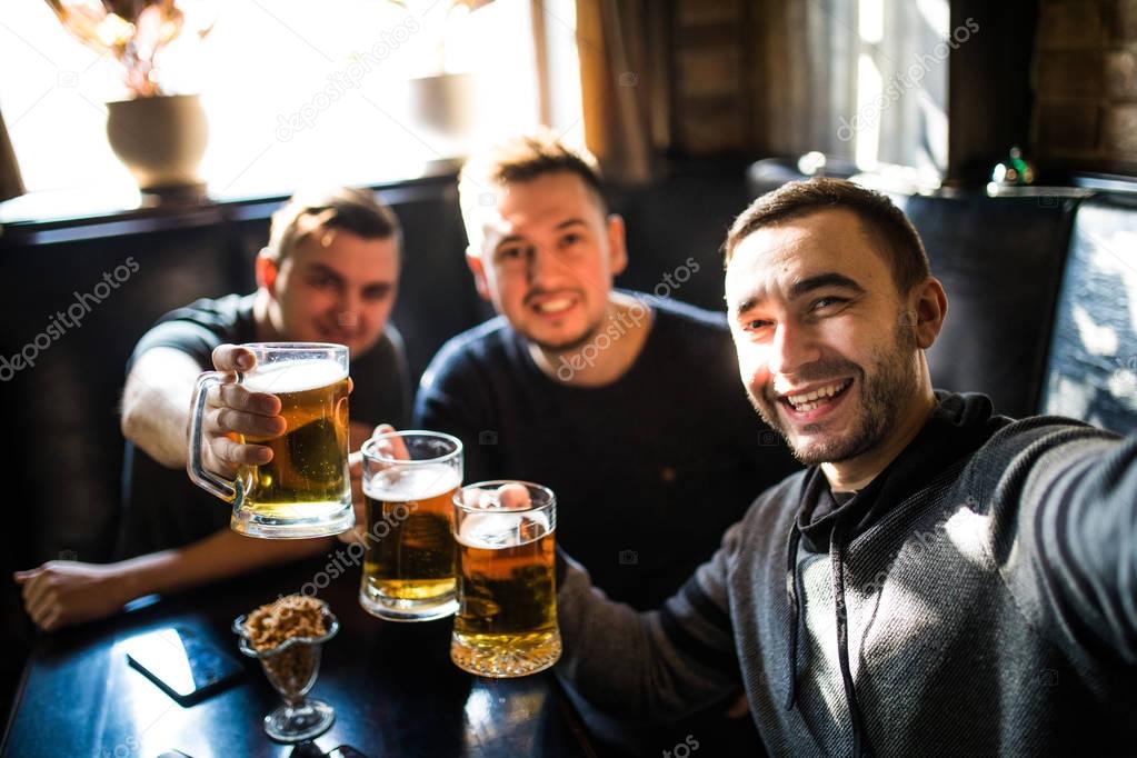 happy male friends drinking beer and taking selfie with smartphone at bar or pub