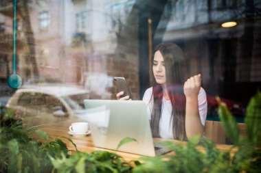Genç kadın telefonda kafede dizüstü bilgisayar önünde söz