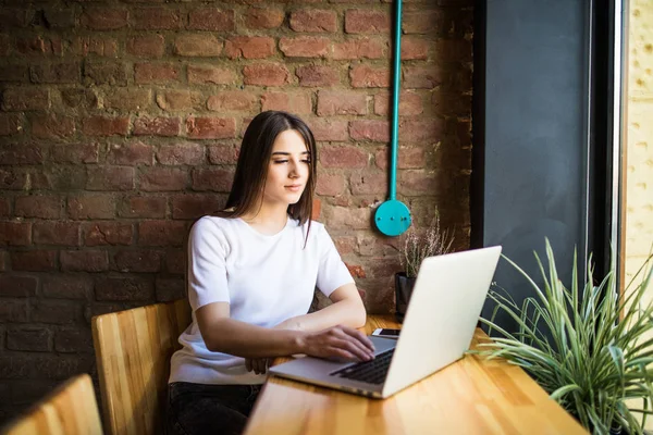 Mujer joven sentada en la cafetería trabajando en el ordenador portátil y mirar la pantalla — Foto de Stock