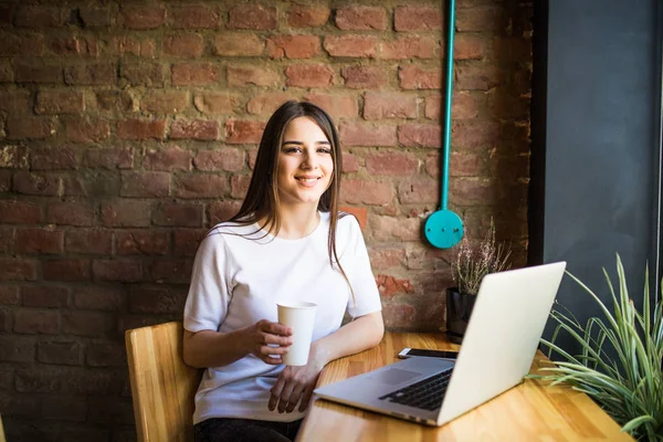 Πορτρέτο του μια νεαρή όμορφη γυναίκα απολαμβάνοντας καφέ κατά τη διάρκεια εργασιών στον υπολογιστή φορητό lap-top, γοητευτικό φοιτήτριας χρησιμοποιώντας net-βιβλίο ενώ κάθονται στην καφετέρια — Φωτογραφία Αρχείου