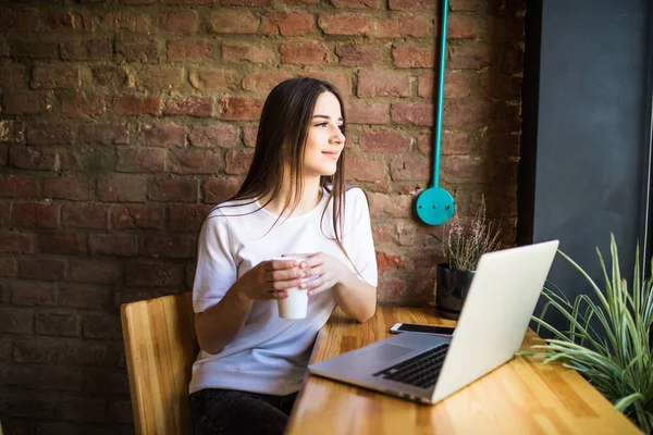 Retrato de una joven hermosa mujer disfrutando del café durante el trabajo en el ordenador portátil, encantadora estudiante usando net-book mientras está sentada en la cafetería — Foto de Stock