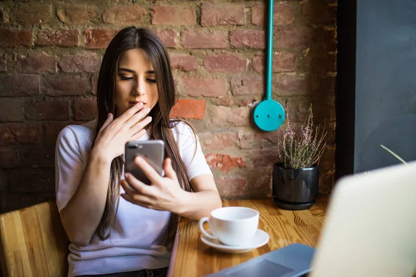 Ung kvinna på café dricka kaffe och använda mobiltelefon i caffee — Stockfoto