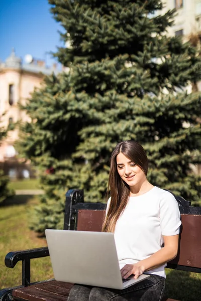 Студентка работает на ноутбуке за пределами офиса на скамейке — стоковое фото