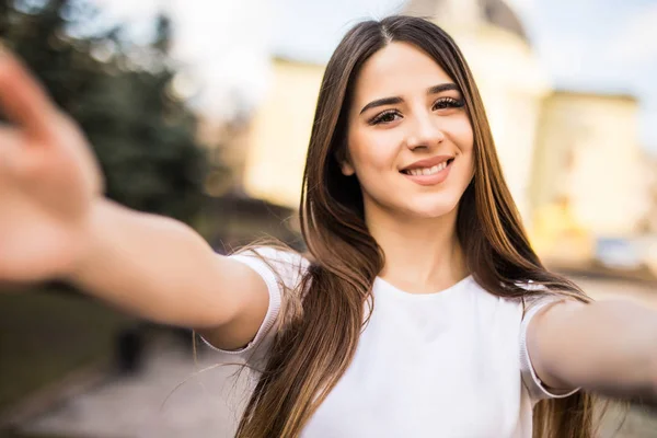 Young beauty woman taking selfie from hands with mobile phone in sunny city street. — Stock Photo, Image