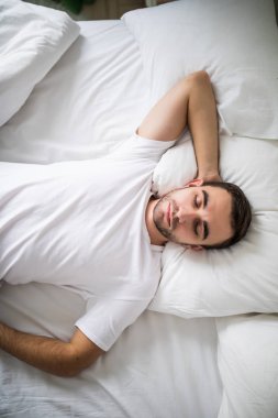Evde beyaz bir yatakta uyumak yukarıda genç bir adam portresi.