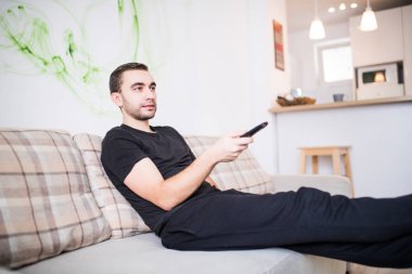 Yakışıklı gülümseyen adam elinde bir uzaktan kumanda ile bir kanepede oturuyor