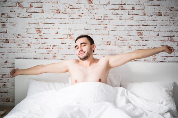 Веселый молодой человек просыпается после сна утром лежа в постели — стоковое фото