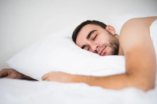 Красивый молодой человек спит в белой кровати в своей комнате дома — стоковое фото