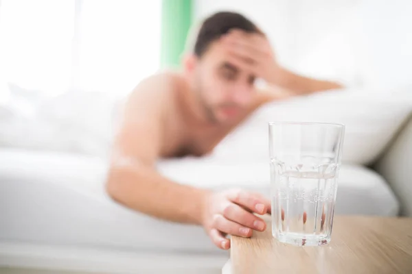 Handsome Man wake up with head pain suffers from headache and extend to get a glass of water in his bed — Stock Photo, Image