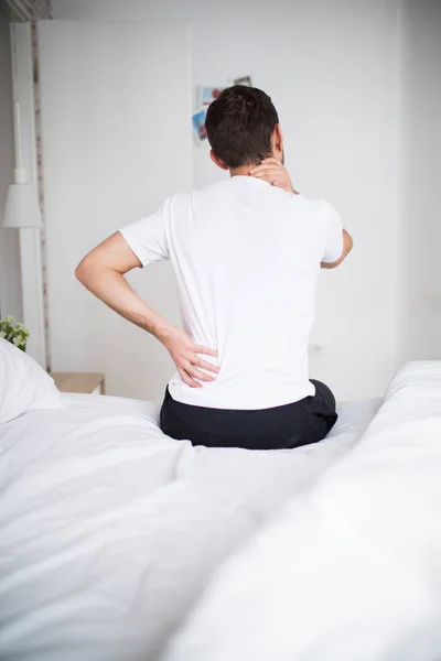 Mann mit Rückenschmerzen zu Hause im Schlafzimmer. Unbequeme Matratze und Kissen verursacht Rückenschmerzen. — Stockfoto