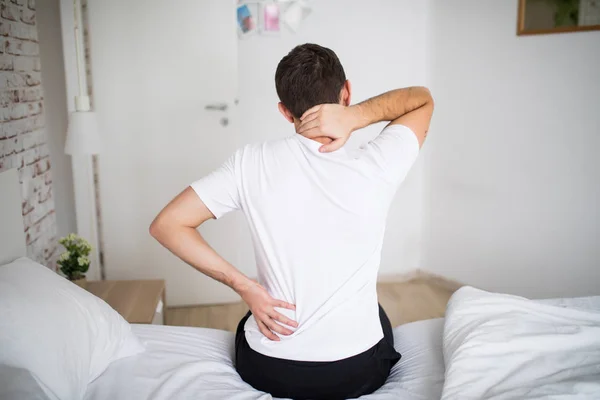 Мужчина, страдающий от болей в спине в спальне. Неудобный матрас и подушка вызывают боль в спине . — стоковое фото